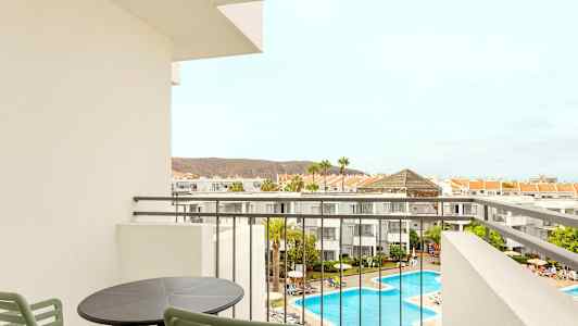 Utsikt från en balkong över hotellområdet med pool och omgivande byggnader. (AI-genererad text)