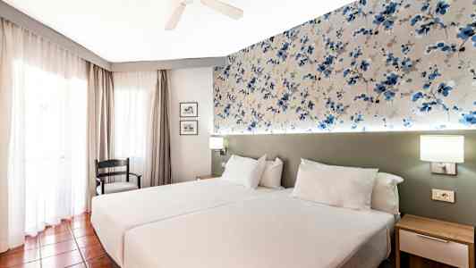 Ett hotellrum med två enkelsängar och mönstrad väggdekoration. (AI-genererad text)