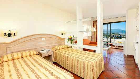 Ett hotellrum med två enkelsängar, en sittgrupp och balkong. (AI-genererad text)