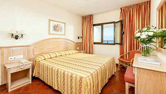 Ett hotellrum med en dubbelsäng, nattduksbord och fönster med havsutsikt. (AI-genererad text)