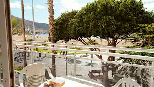 Utsikt från en balkong mot en strand med palmer och träd. (AI-genererad text)