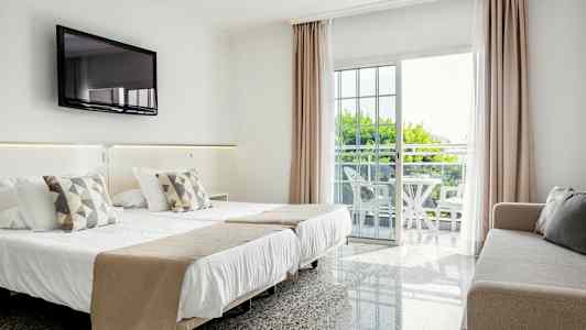 Hotellrum med dubbelsäng, soffa, väggmonterad TV och balkong med sittmöbler. (AI-genererad text)