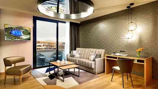 Modernt vardagsrum med soffgrupp, ett skrivbord och utsikt mot en balkong. (AI-genererad text)