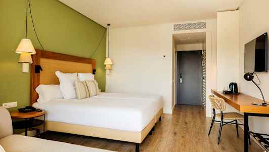 Hotellrum med en bred säng, skrivbord och grön vägg. (AI-genererad text)