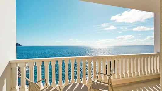 Utsikt från en balkong med bord och stolar mot havet. (AI-genererad text)