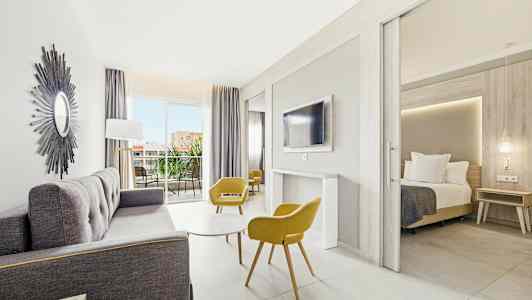 Ljust och modernt hotellrum med sittgrupp, sovrum och balkong. (AI-genererad text)