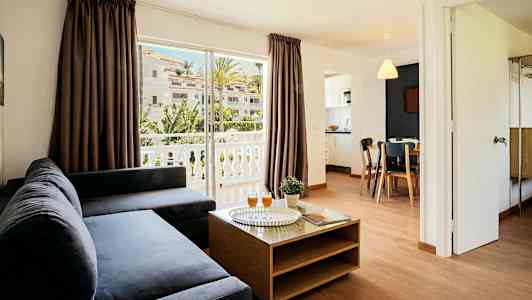 Ett vardagsrum med mörk soffa, ett soffbord och utsikt över en balkong med grönska. (AI-genererad text)