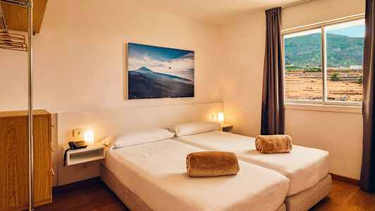 Ett hotellrum med två enkelsängar, ett fönster med utsikt över landskapet och en tavla på väggen. (AI-genererad text)