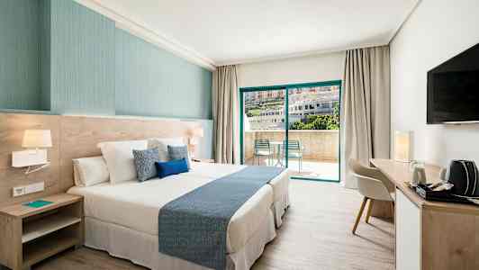 Ett hotellrum med en stor säng, modern inredning, ett skrivbord och stora skjutdörrar som leder till en balkong. (AI-genererad text)