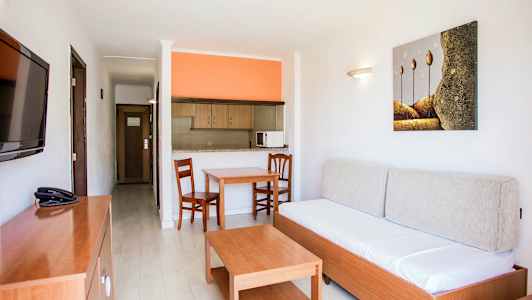 Lägenhetsinteriör med en soffa, ett bord, två stolar och ett öppet kök med orange vägg. (AI-genererad text)