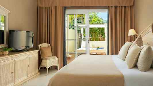 Ett hotellrum med en säng, en TV på en byrå och en stol. Glasdörrar leder till en uteplats med sittmöbler. (AI-genererad text)