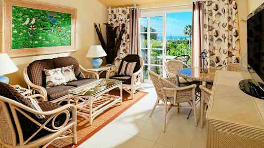 Ett vardagsrum med rottingmöbler, ett glasbord och en färgglad tavla på väggen. (AI-genererad text)