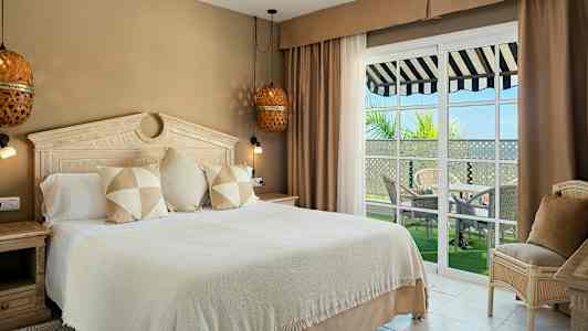 Ett hotellrum med en stor säng, smakfull inredning och fönster mot en balkong med utsikt. (AI-genererad text)