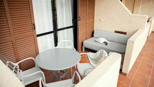 En rymlig terrass med vita stolar runt ett runt bord och en grå soffa. (AI-genererad text)