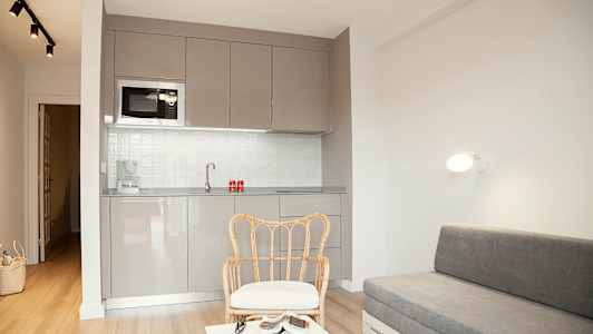 Ett modernt rum med grått kök, rottingstol och grå soffa. (AI-genererad text)