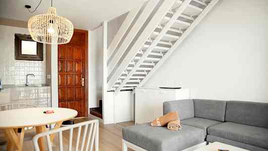 Inomhusvy med vardagsrum, köksområde och trappor i vit och träinredning. (AI-genererad text)