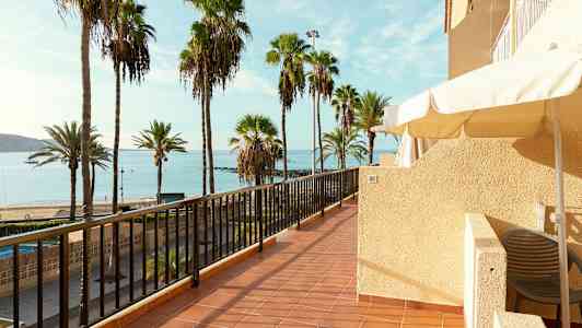 Bild av en terrass med utsikt över en strand med palmer och hav. (AI-genererad text)