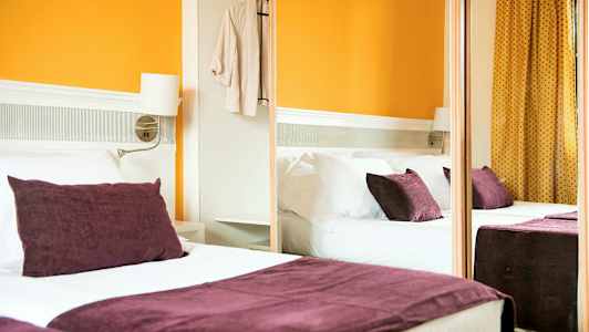 Ett hotellrum med en dubbelsäng, lila kuddar och orange väggar. (AI-genererad text)