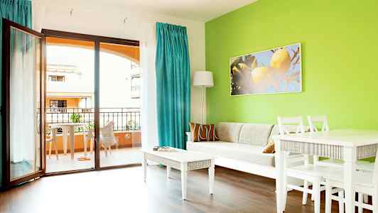 Vardagsrum med grön vägg, vit soffa, vita möbler och utsikt mot balkong. (AI-genererad text)