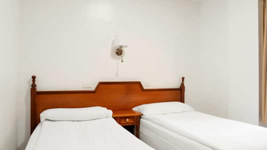 Två enkelsängar med vita lakan och träsänggavlar står bredvid varandra. (AI-genererad text)