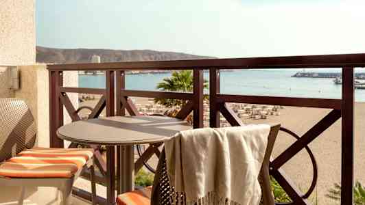 Balkong med bord och två stolar samt utsikt över stranden och havet. (AI-genererad text)