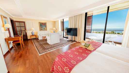 Ett rymligt hotellrum med dubbelsäng, sittgrupp, skrivbord och en balkong med utsikt. (AI-genererad text)