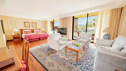 Ett hotellrum med en säng, sittmöbler och en balkong med utsikt. (AI-genererad text)