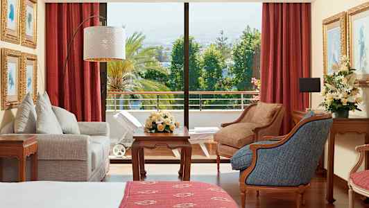 Ett hotellrum med möbler, blommor och utsikt över en grönskande balkong. (AI-genererad text)