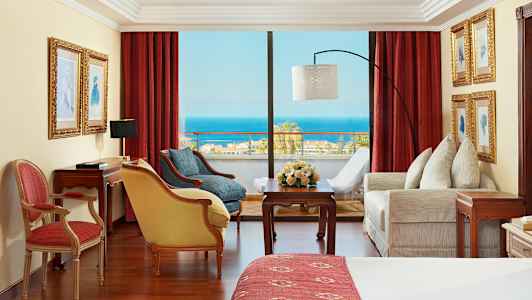 Rum med röda gardiner, möbler och utsikt över havet. (AI-genererad text)