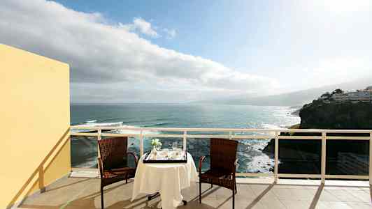 Två stolar och ett bord med duk står på en terrass med utsikt över havet. (AI-genererad text)