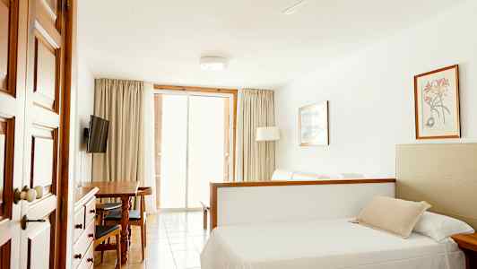 Ett rum med en säng, matbord, TV och glasdörrar som leder ut till balkongen. (AI-genererad text)