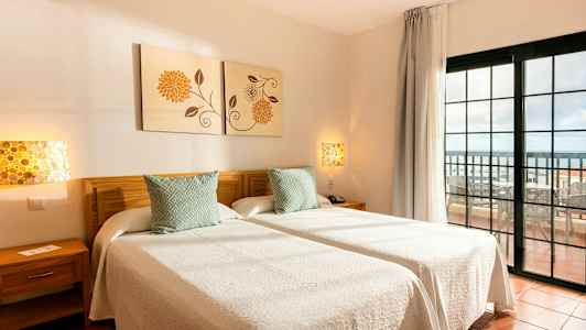 Två enkelsängar med vita sängkläder i ett rum med utsikt mot en balkong. (AI-genererad text)