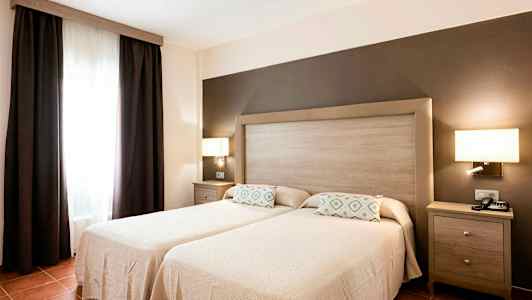 Ett sovrum med två enkelsängar, en gemensam huvudgavel och mörka gardiner vid ett fönster. (AI-genererad text)