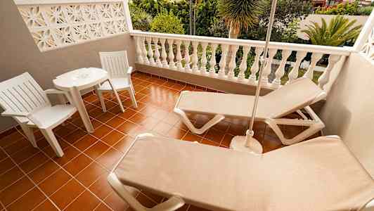 En terrass med två solstolar, ett bord och två stolar med utsikt över grönskande omgivningar. (AI-genererad text)