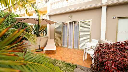 Utomhusterrass med solsäng, parasoll och bord med stolar, omgiven av vegetation. (AI-genererad text)