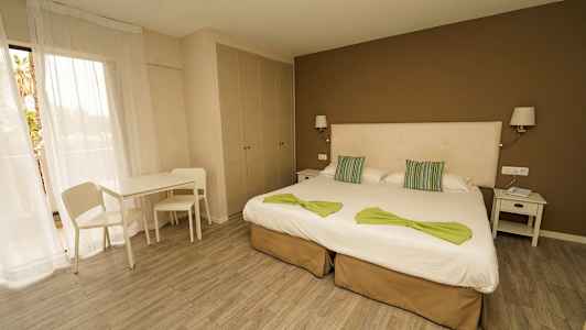 Ett hotellrum med två enkelsängar, nattduksbord, bord, stolar och en garderob. (AI-genererad text)