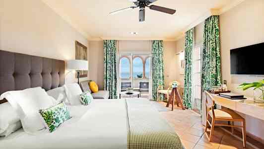 Ett hotellrum med en stor säng, sittgrupp, arbetsbord och havsutsikt genom fönstret. (AI-genererad text)