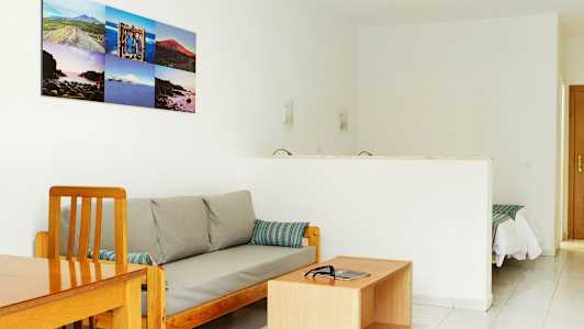 Ett vardagsrum med en soffa och ett soffbord, samt en öppning mot ett sovrum. (AI-genererad text)