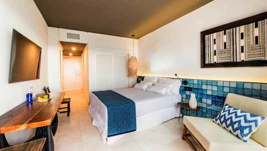 Modern hotellrum med dubbelsäng, bord med frukt och en stol. (AI-genererad text)