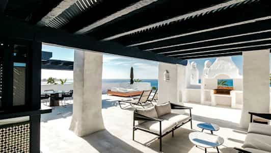 Solig terrass med vita väggar, svart träbjälkar och modern lounge möbler. (AI-genererad text)