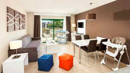 Ett modernt vardagsrum med soffa, matbord, barnstol och utsikt mot en balkong. (AI-genererad text)