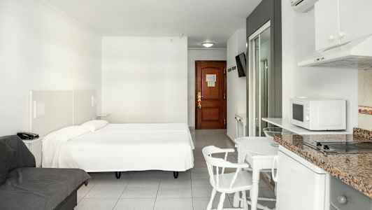 Ett hotellrum med en dubbelsäng, en soffa, matbord med stolar och ett pentry. (AI-genererad text)