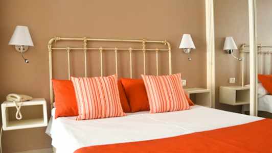 Ett hotellrum med en säng klädd i vita och röda sängkläder, omgivna av vägglampor. (AI-genererad text)