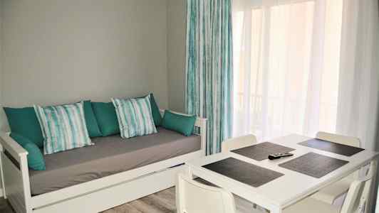 Vardagsrum med vit dagbädd och matbord med fyra stolar. (AI-genererad text)