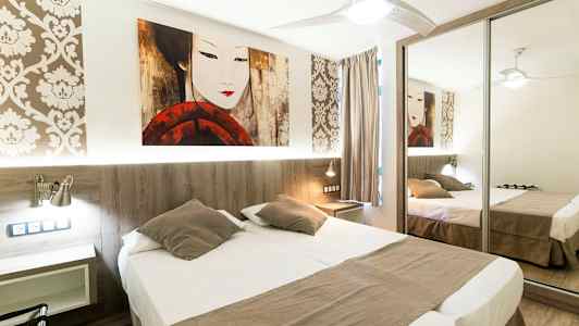 Ett hotellrum med en dubbelsäng, spegelgarderob och dekorativ väggtapet. (AI-genererad text)