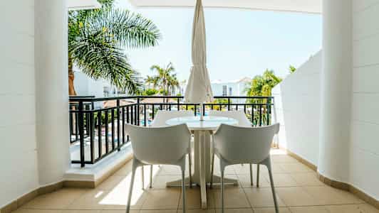 En möblerad balkong med utsikt över palmträd och en byggnad. (AI-genererad text)