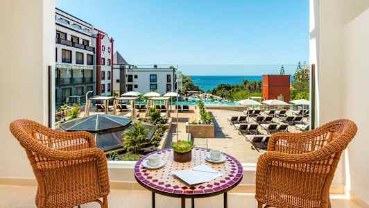 Utsikt från en balkong över en hotellpool med solstolar och havet i bakgrunden. (AI-genererad text)