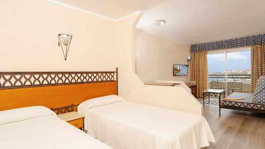 Hotellrum med två enkelsängar, sittgrupp och balkong. (AI-genererad text)