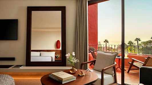 Ett elegant hotellrum med en spegel, öppning mot en möblerad terrass och havsutsikt. (AI-genererad text)