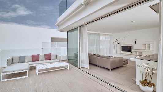 En ljus terrass med soffmöbler och utsikt till ett modernt vardagsrum med glasväggar. (AI-genererad text)